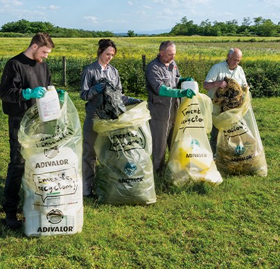 Quatre personnes rassemblant des sacs de collecte A.D.I.VALOR en bordure de parcelle